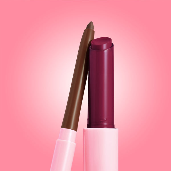 Juicy Berry ColourPop So Juicy Plumping Lip Liner & Balm Set showing a retractable brown lip liner poised to line and a twist-up berry plum balm bullet in a pink tube, standing side by side on a soft pink gradient background.