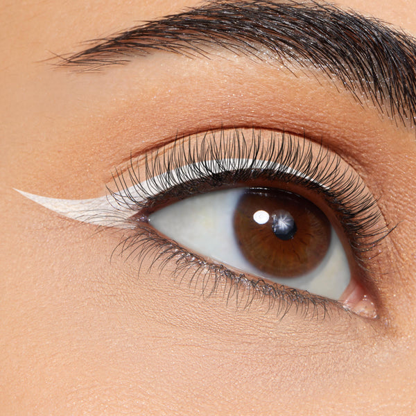 Crisp white winged liner sweeping from the upper lash line, created with ColourPop BFF Liquid Liner in Graceland, on a close-up brown eye with long lashes, neutral matte shadow, and a sharp cat-eye flick.