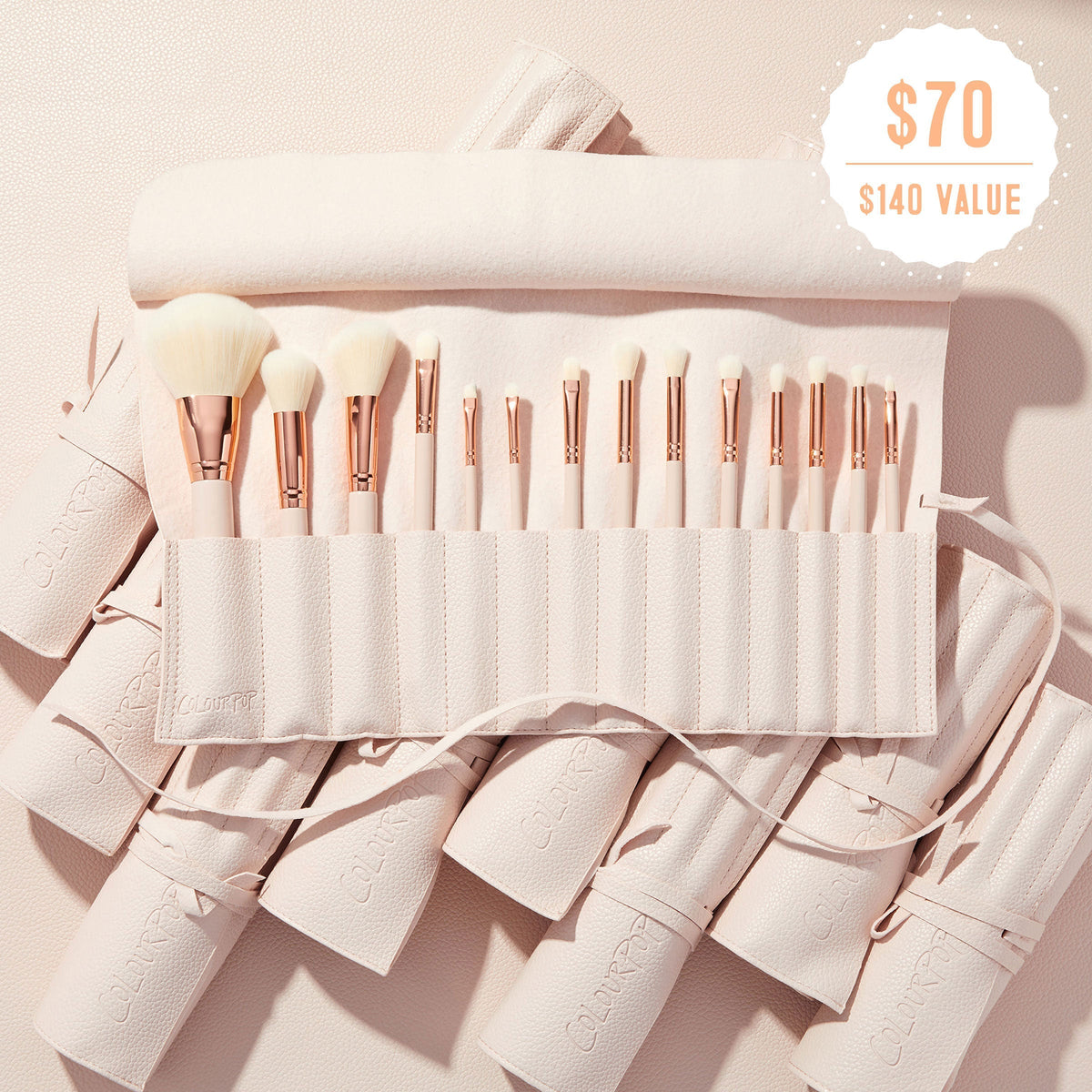 Sweet Fantasy ColourPop Shadow Palette & Brush Set brush roll opens to reveal soft white-bristle face and eye brushes with rose-gold ferrules, arranged in a blush-pink travel case on a textured nude surface, with a $70 ($140 value) badge.