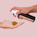 Tanning Mitt catching a pump of golden tanning foam from a black pump bottle, illustrating application for a streak-free sunless tan on a blush pink background, part of ColourPop Makeup Tools & Accessories.