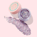 Open jar of Moon Prism Power ColourPop Glitter Gel showing chunky iridescent lavender flakes and star confetti, with a wide swatch spread beside it; peach lid with teal “Glitterally Obsessed” logo on a pale pink background.