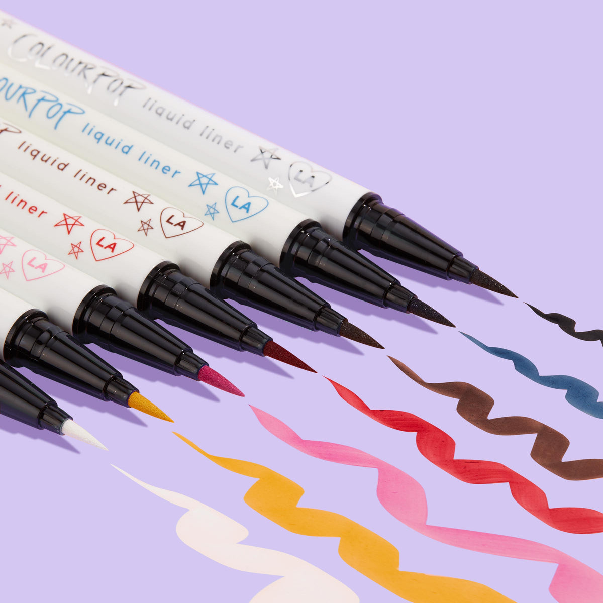 ColourPop Graceland BFF Liquid Liner creates a bold white squiggle beside multicolor swatches, the feltβtip pen and doodled white barrel angled on a lavender background, showcasing precise application and opaque, quickβdry wear.
