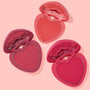 Three heart-shaped blush compacts open to reveal matte pans in coral, rose, and fuchsia, arranged diagonally on a pale pink background; Heart to Heart ColourPop Heart Powder Blush Set for buildable cheek color.