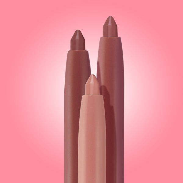 Three chubby lip liners in nude, rose, and mauve stand upright with pointed tips against a pink gradient backdrop, highlighting the Lips Don’t Lie ColourPop So Juicy Plumping Lip Liner Set, a trio for precise, plumped-looking lips.