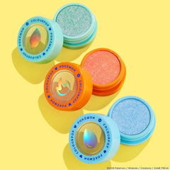 Solar Beam Super Shock Shadow by ColourPop, an open mint-green shimmer pan in an aqua pot, sits beside coral and icy blue companion shades with holographic leaf, flame, and water icons, arranged in a bright yellow flat lay from the Pokémon collection.
