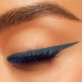 Winged eyeliner creates a sharp cat-eye on a closed eyelid, showcasing ColourPop Crème Gel Liner Out of the Blue - a metallic navy-blue shimmer - gliding smoothly along the lash line with vivid blue lashes in a close-up studio beauty shot.