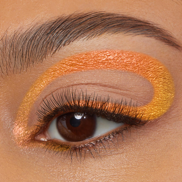 Looping graphic eyeliner tracing the crease and lower lash line in a vivid orange-to-gold chrome finish on a macro eye, showcasing Movie Star, the ColourPop Chrome Crème Gel Liner, with long lashes and a groomed brow.