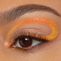Chrome Hearted ColourPop Chrome Crème Gel Liner sweeps in a bold metallic orange-to-gold loop over and under a brown eye, accenting long lashes in a crisp studio close-up beauty shot.