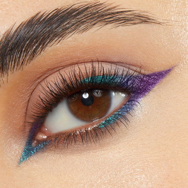 Graphic winged liner accents a brown eye, with metallic teal along upper and lower lash lines and a sharp purple outer flick, showcasing Power Trip, a ColourPop Chrome Crème Gel Liner, in a close-up on neutral skin with defined lashes.