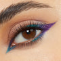 Graphic winged liner accents a brown eye, with metallic teal along upper and lower lash lines and a sharp purple outer flick, showcasing Power Trip, a ColourPop Chrome Crème Gel Liner, in a close-up on neutral skin with defined lashes.