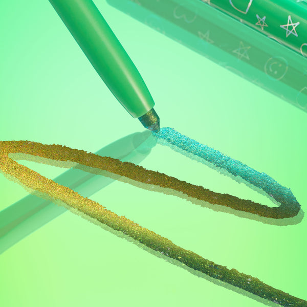 Wild Idea pencil draws a vivid teal-to-gold duochrome line across a glossy green surface, showcasing creamy metallic payoff; ColourPop Chrome Crème Gel Liner with star-and-heart printed barrel shown in a stylized close-up.