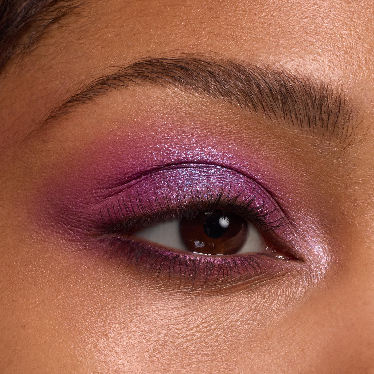 Shimmery violet‑magenta eyeshadow blends across the lid, crease, and lower lash line with a metallic inner‑corner highlight, showcasing the It’s My Pleasure ColourPop Shadow Palette in a tight macro of the eye and groomed brow.