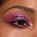 Shimmering fuchsia-to-lilac eyeshadow glows on a brown eye, blended across lid and crease with an inner-corner highlight, showcasing the Rainbow Rush ColourPop Shadow Palette Set in a studio close-up with groomed brow and soft lighting.