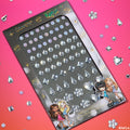 ColourPop Crystal Face Jewels - Individual Face and Hair Crystals sheet displays adhesive rhinestones in round, square, teardrop, heart, and flower shapes, arranged in rows on a Bratz-themed card, set on a pink gradient flat lay with scattered gems.