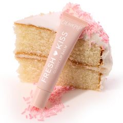 Blush pink ColourPop Fresh Kiss tube leans on a vanilla cake slice with white frosting and pink sprinkles, spotlighting the Sweet Treats ColourPop Glossy Lip Balm Trio in a playful dessert-themed product shot.