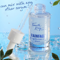 Rainfall 2% hyaluronic acid face serum bottle by Fourth Ray Beauty sits open with a glass dropper, water splashing on a blue background with green leaves; Remedy + Rainfall ColourPop Face Serum, shown with a claim it can mix with other serums.
