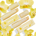 Vanilla Kisses Lip Care Set showcases ColourPop Lip Scrub and lip balm, tubes uncapped to reveal product, in soft-yellow Fourth Ray Beauty packaging with orchid graphics, arranged flat on a white background among yellow orchid flowers.