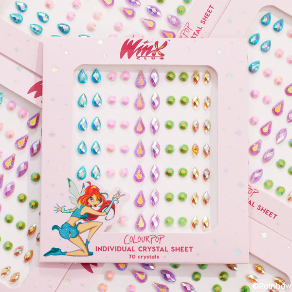ColourPop Crystal Face Jewels Individual sheet sparkles in a pink Winx Club box, showing 70 self-adhesive gems in teardrop, round, and diamond shapes - iridescent blues, pinks, greens, and gold - flatlay of overlapping packs for festival makeup.
