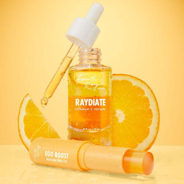 Get That Glow ColourPop Face Set with Fourth Ray Beauty Raydiate Vitamin C Serum and a dripping dropper beside Ego Boost Brightening Serum Stick, styled on a wet glossy surface with fresh orange slices and a warm golden backdrop.