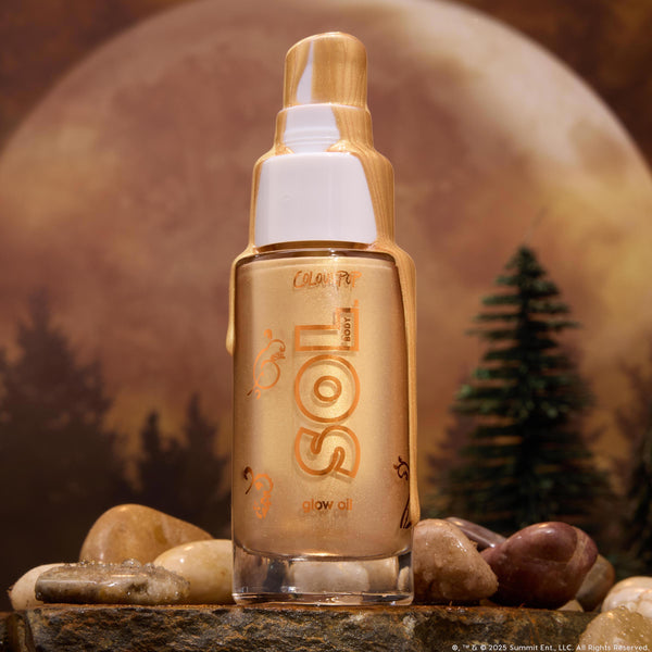 ColourPop SOL Glow Oil - It’s a Wolf Thing - standing upright with molten gold drips over a white pump, warm-bronze shimmer glowing through the glass bottle, set on dewy rocks by pine trees under a full moon, evoking a moody forest vibe.