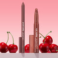 ColourPop Lippie Stix + Pencil Set Big Smooch stands uncapped, revealing a rosy brown lipstick and matching liner with caps nearby, styled among glossy cherries against a soft pink gradient backdrop.