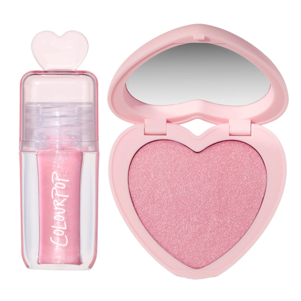 Heart to Get 2 Good 4 U blush and UGL set featuring a shimmery pink liquid lip gloss with a heart-shaped cap beside a matching sparkly pink heart-shaped powder blush compact with mirror on a clean white background.