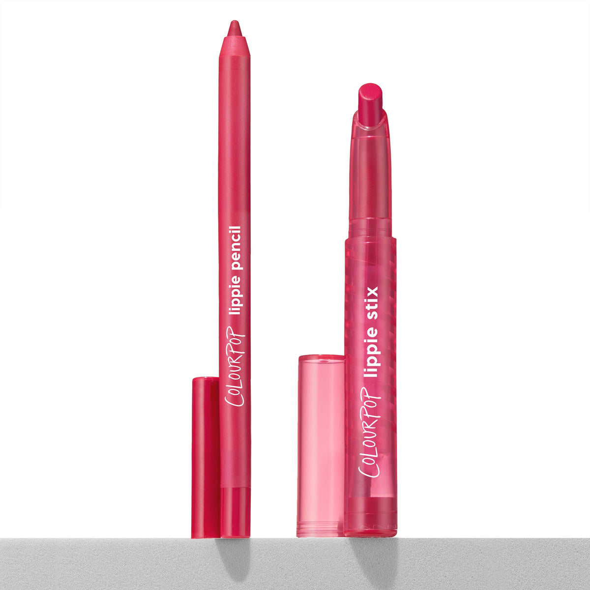 Ultimate Lip Combo ColourPop Lippie Stix + Pencil Set stands upright with caps off, revealing a creamy fuchsia liner and matching twist-up lipstick bullet in translucent pink tubes on a light shelf against a white background.