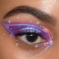 ColourPop BFF Liquid Liner in Graceland drawing a crisp white graphic wing across a close-up eye, layered over iridescent purple shimmer shadow with sparkles and heart doodles, highlighting precise payoff and clean edges.