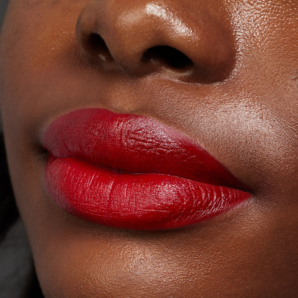 Bold red lips wearing Va Va Voom, lined and filled with the ColourPop Lippie Stix + Pencil Set, showing a creamy satin finish and crisp definition; tight beauty close-up on deep brown skin emphasizing rich pigment and smooth texture.