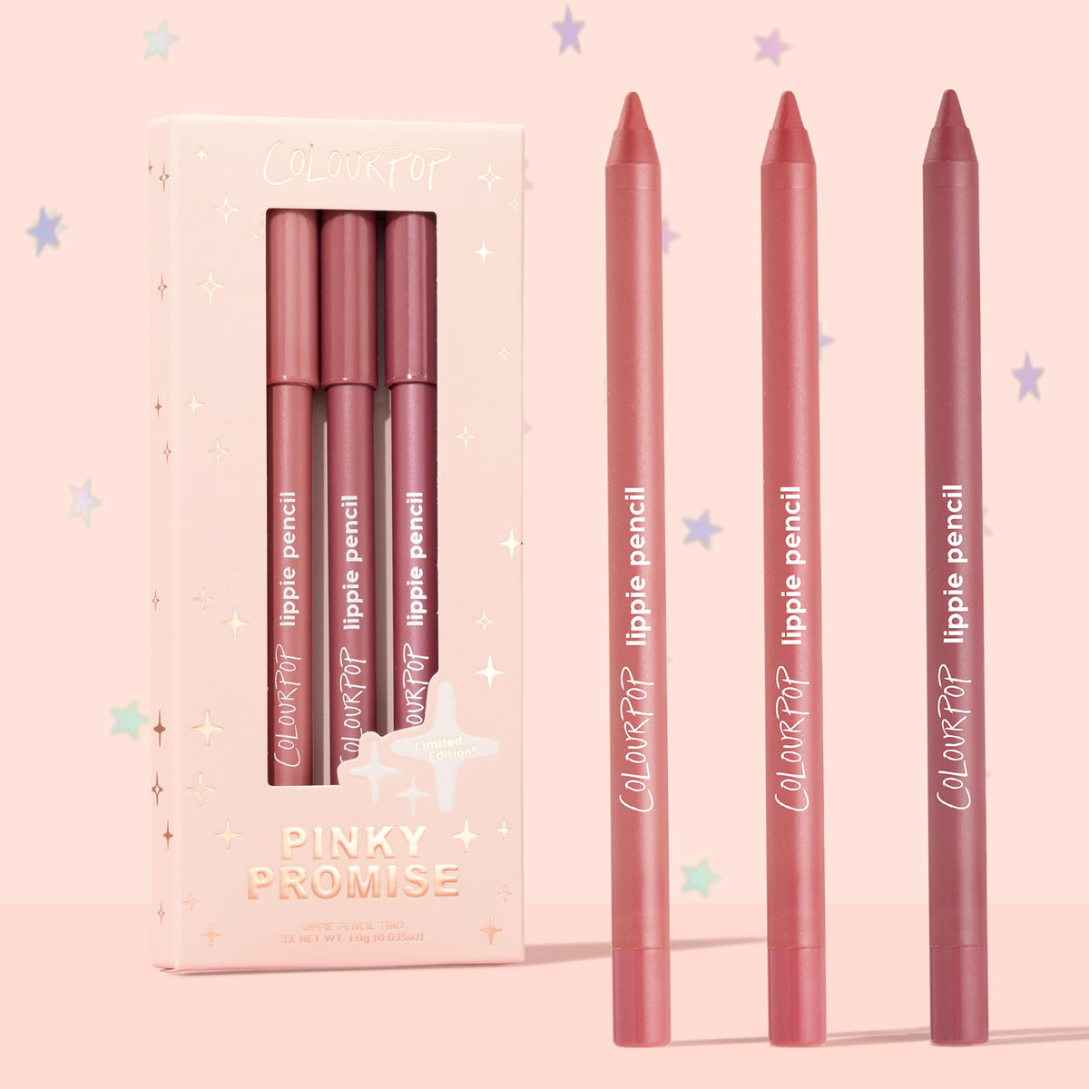 Pinky Promise ColourPop Lippie Pencil trio stands upright, three creamy lip liners in nude pink, rosy coral, and mauve berry beside a blush, star-embossed box on a pastel pink backdrop, limited edition set.