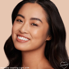 Light 60 N shade of ColourPop Hyaluronic Hydrating Foundation delivering a dewy, natural finish - model smiling in close-up with smooth, even coverage - studio shot on a warm beige background highlighting skin glow and texture.