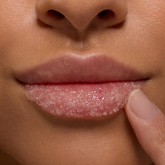 Close-up lips exfoliating with ColourPop Lip Scrub, Vanilla Cake; a fingertip massages the gritty sugar crystals across the lower lip in a studio beauty close-up.
