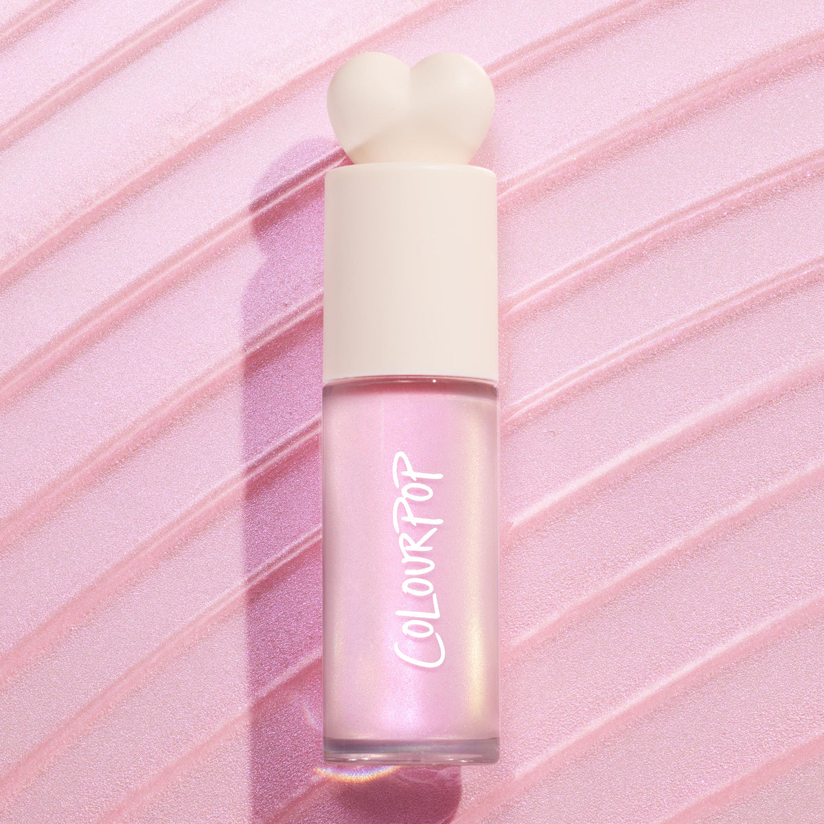 ColourPop Liquid Highlighter Pink Pony bottle standing upright, frosted glass tube glowing iridescent pink-gold with a cream heart-shaped cap, set against a diagonally swiped, shimmering pastel pink background.