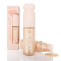 ColourPop Liquid Highlighter Sugar Donut bottle stands capped with a blush heart-shaped top, while an open vial pours dewy pearly champagne glow; a peach box labeled liquid hi-lite sits behind on a white studio background.