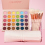 Crazy For Hue ColourPop Shadow Palette & Brush Set displays a 30-pan matte rainbow palette with an open pink lid, paired with soft white-bristle brushes with rose-gold ferrules in a clear cup and a pale pink embossed brush roll, styled on a pink backdrop.