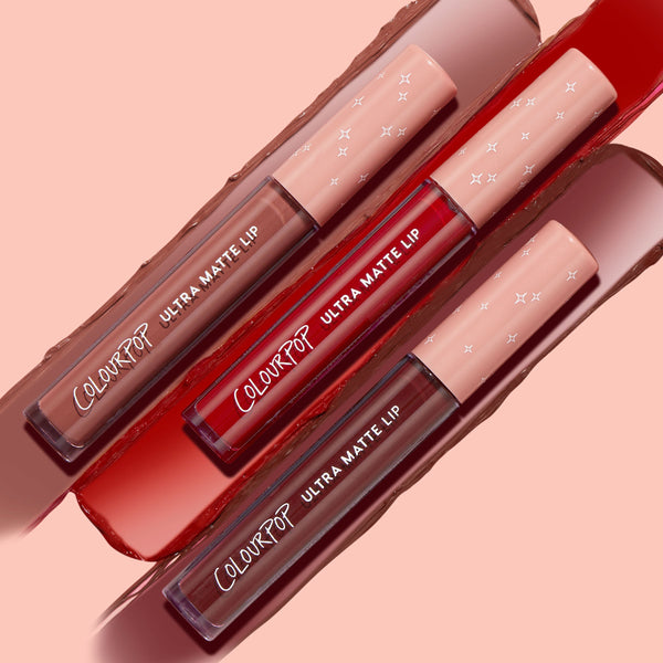 Three ColourPop Ultra Matte Lip tubes from the Matte Babe set - nude, classic red, and deep berry - lay diagonally with matching swatches on a peach backdrop, pink star-print caps visible, highlighting long-wear ultra matte liquid lipstick shades.