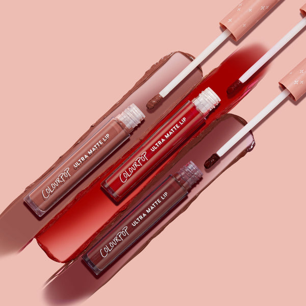 Three ColourPop Ultra Matte Lip tubes from the Matte Babe bundle sweep nude, bright red, and deep berry swatches with doe‑foot applicators on a blush pink backdrop, highlighting the long‑wear ultra matte finish.
