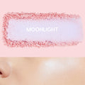 Moonlight ColourPop Pressed Powder Highlighter swatch spreads icy lavender with pink edges, while a nearby cheek glows with its pearly sheen, set on a pastel pink background to show color payoff and luminous finish.
