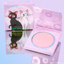 ColourPop Moonlight pressed powder highlighter compact showing a soft pink pan, open beside its box with Sailor Moon’s Luna and Artemis artwork, on a reflective lavender surface, pastel packaging with moons and stars; ColourPop Pressed Powder Highlighter.
