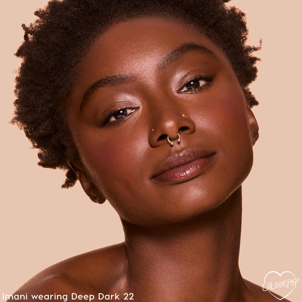 Model wears ColourPop Pretty Fresh Tinted Foundation Balm in Deep Dark 22, showcasing dewy, even coverage and natural glow in a close-up against a warm beige background for accurate shade reference.