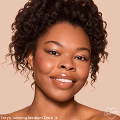 Model smiles wearing ColourPop Pretty Fresh Tinted Foundation Balm in Medium Dark 16, showing smooth, dewy, medium coverage in a close-up studio shot against a beige background with soft blush and glossy lips.