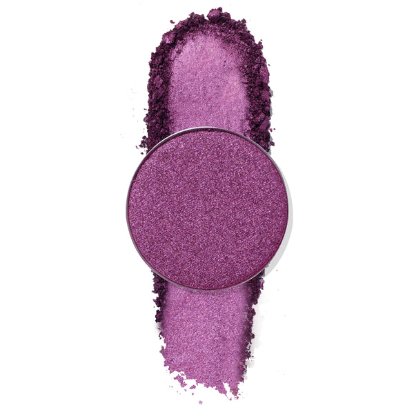 Round pan of ColourPop Paradiso Pressed Powder Shadow sits over a bold swipe of crushed metallic orchid-purple shimmer on a white background, showcasing the vibrant, buildable eyeshadow color payoff.