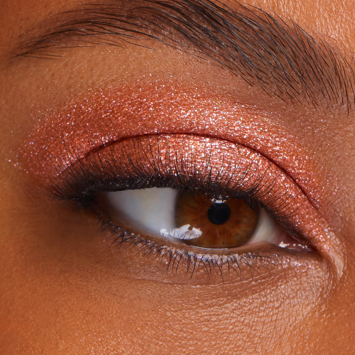 Shimmering copper eyeshadow coats a brown eye, showcasing Flamethrower, a metallic shade of ColourPop Super Shock Shadow, with glittery payoff swept across the lid and crease, accenting soft lashes and skin texture in a tight beauty close-up.