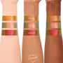 ColourPop Shadow Stix in Wolf Girl swatched on three arms (light, medium, deep); top stripe shifts green to gold-orange. Lower stripes show It’s Always Been Him (peachy pink with teal shift) and Vampire Girl (red with green shift) for comparison.