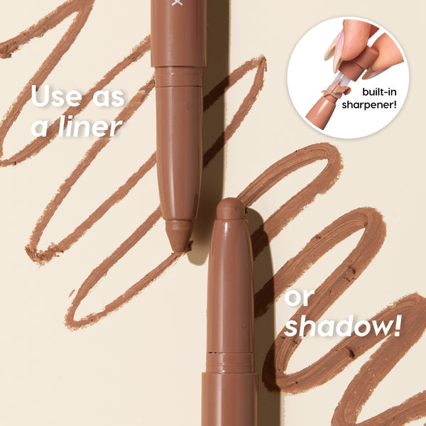 Two ColourPop Shadow Stix in Ghouls Night Out draw smooth cocoa-brown lines on a beige surface, with an inset hand showing the built-in sharpener - wearable as eyeliner or eyeshadow.