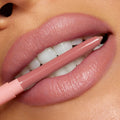 ColourPop So Juicy Plumping Lip Liner with Peptides in Love That lines plush, glossy lips, the rosy‑nude pencil held between teeth to showcase its precise tip and creamy payoff in a clean studio close‑up.