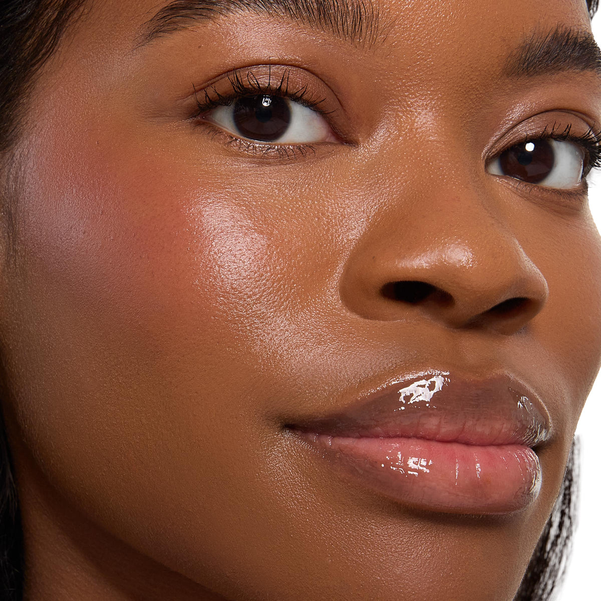 ColourPop Cream Blush Crowd Favorite adds a soft rosy flush on the model’s cheek, blended with a dewy, skin-like sheen; extreme close-up shows smooth deep complexion, natural lashes, and glossy lips, highlighting the product’s radiant finish.