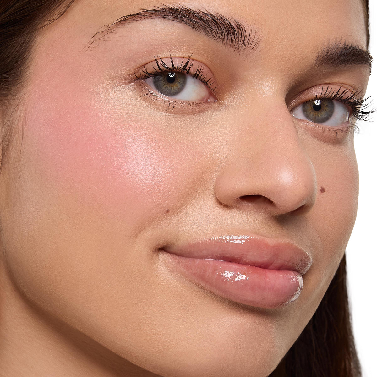 Crowd Favorite ColourPop Cream Blush melts into skin, giving a soft pink, dewy flush on a model’s cheek; close-up face shows blended pigment with natural glow, long lashes, and glossy lips against a white background.