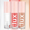 Three ColourPop Lux Lip Oil tubes stand side by side in the Top Hits bundle, displaying clear, coral pink, and warm nude shades with pink star-print caps against a soft pastel backdrop.