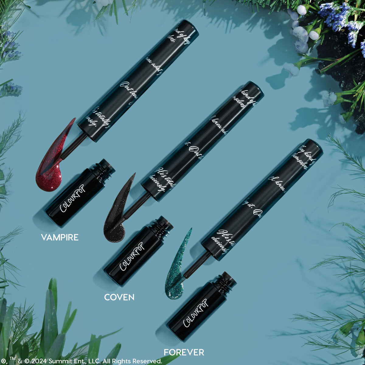 ColourPop Graphix Ink Liner in Forever swatched as a sparkling teal wing, with open tube and fine brush applicator; two companion shades, Vampire (red) and Coven (black), rest nearby on a blue backdrop with greenery.